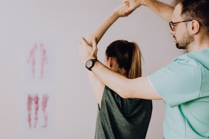 Chiropracteur portant des lunettes examinant le bras levé d'une patiente dans son cabinet médical
